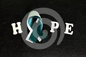 Top view of with word hope teal and white ribbon in dark black background. Cervical cancer hope and awareness concept.