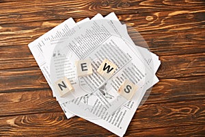 top view of word news made of alphabet cubes on heap of newspapers on wooden background