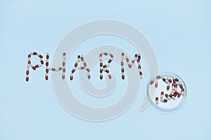 Top view of word PHARM laid out on blue backdrop and Petri dish with medical capsules. Copy space. World Pharmacist Day