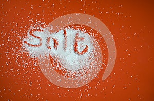 Top view of the word salt writter in spilled white salt on a red backgroud with copy space photo