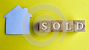 Top view of word SOLD and model paper house with yellow background.