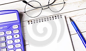 Top view of work desk with glasses, blue calculator, pen and blank notepad with space to insert text. Business concept