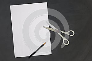 Top View of Work Space on Black Chalk Board with White Paper Pencil and Scissors