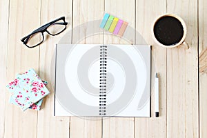 Top view of working desk with blank notebook with pen, coffee cup, colorful note pad and eyeglasses on wooden background