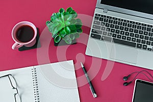 Top view of workplace with laptop, notebook with pen and other items on desktop with burgundy surface