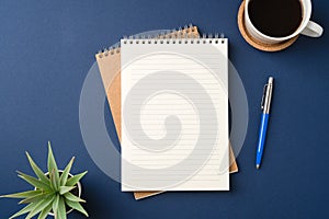 Top view of a workspace with a blank notebook, pen, coffee, and plant