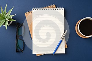 Top view of a workspace with a blank notebook, pen, glasses, coffee, and plant