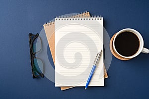 Top view of a workspace with a blank notebook, pen, glasses, coffee, and plant