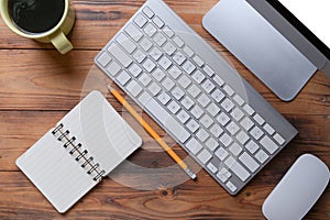 Top view workspace with computer, wireless keyboard, notebook and coffee cup on wooden desk.