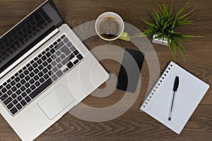 Top view of workspace. Table desk with laptop, cell phone, coffee, notepad, pen and plant with empty space background for design.