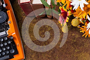 Top view of workspace of vintage orange typewriter and on bouquet of orange summer flowers