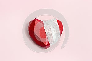 Top view with wounded heart red. Bandaged polygonal paper heart on pink background