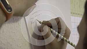 Top view of writing hand of manager sitting at the table. Stock. Writing with a pencil on a white sheet of paper