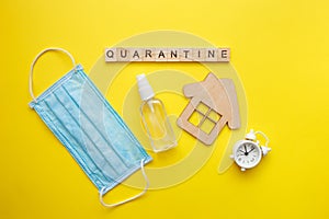 Top view of a yellow background with the word quarantine. Protective medical mask, alcohol spray and wooden house. Respiratory