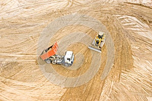 Top view of yellow bulldozer and dump truck working at construction site