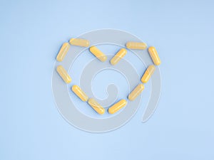 Top view of yellow capsule pills heart shape on a light blue background.