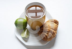 A top view of a yellow cup with Colombian traditional hot drink knowed as AGUA DE PANELA with lemon, one bread and white backgroun