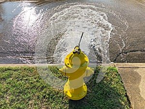 Top view yellow fire hydrant gushing water across a residential street near Dallas, Texas, USA