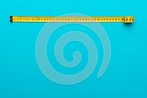 Top view of yellow measuring tape over turquoise blue background with copy space