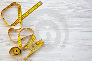 Top view, yellow measuring tape on white wooden background. From above.