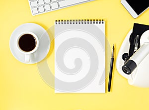 Top view of yellow office desktop with microscope, notepad, computer, smartphone. Mock up, empty space, science template