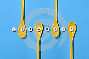 top view of yellow plastic spoons and pills with vitamine lettering in row