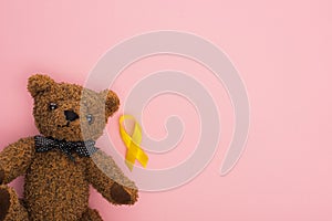 Top view of yellow ribbon near teddy bear on pink background, international childhood cancer day concept. photo