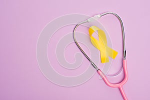Top view of yellow ribbon and pink stethoscope on violet background, international childhood cancer day concept. photo