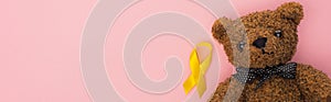 Top view of yellow ribbon and teddy bear on pink background, panoramic shot, international childhood cancer day concept. photo