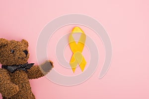 Top view of yellow ribbon and toy on pink background, international childhood cancer day concept. photo