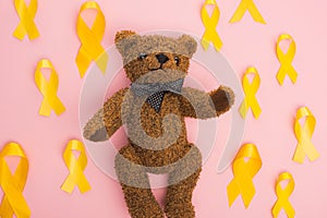 Top view of yellow ribbons around teddy bear on pink background, international childhood cancer day concept. photo