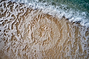 Top view of yellow sandy beach with white foam waves.