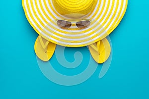 Top view of yellow sunglasses, striped retro hat and flip-flops