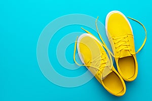 Top view of yellow untied sneakers on blue turquoise background with copy space