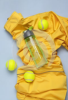 Top view of yellow wind breaker,tennis balls,bottle of water on the blue background.Vertical image.Sport fashion and clothes