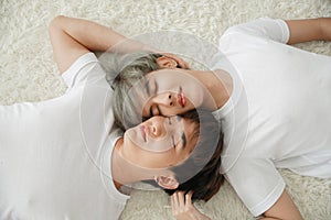 Top view of young Asian gay couple closed their eyes and lying on floor with white fluffy carpet. Their men face are very close to