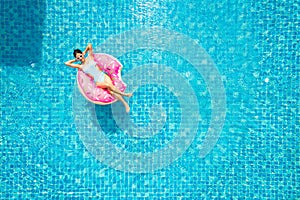 Top view of young asian woman in swimsuit on the pink donut lilo in the swimming pool