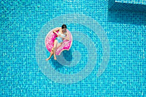 Top view of young asian woman in swimsuit on the pink donut lilo in the swimming pool