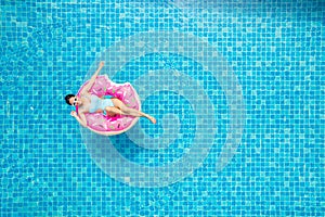 Top view of young asian woman in swimsuit on the pink donut lilo in the swimming pool