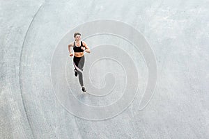 Top view of young attractive athletic woman speed running on city asphalt and workout in the morning time on a sunny summer day.