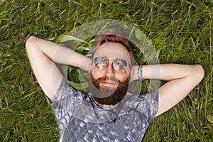 Portrait of a young handsome bearded man relaxing on the grass with his hands under the head