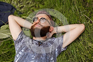 Top view of a young bearded man relaxing on the grass with his hands under the head