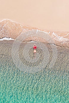 Top view. Young beautiful woman in a red hat and bikini lying and sunbathe in sea water on the sand beach. Drone, copter photo.