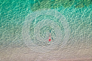 Top view. Young beautiful woman in a red hat and bikini lying and sunbathe in sea water on the sand beach. Drone, copter photo.