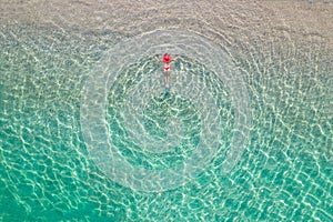 Top view. Young beautiful woman in a red hat and bikini lying and sunbathe in sea water on the sand beach. Drone, copter photo.