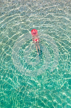 Top view. Young beautiful woman in a red hat and bikini swimming in sea water on the sand beach. Drone, copter photo. Summer
