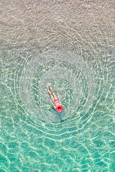 Top view. Young beautiful woman in a red hat and bikini swimming in sea water on the sand beach. Drone, copter photo. Summer