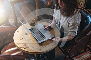 Top view, young business woman in white shirt sitting at desk and working online on laptop while using smartphone