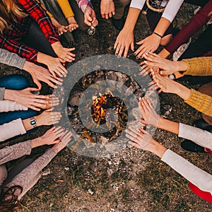 Top view of young campers sitting around and warming their hands on a campfire in the fall.