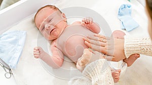 Top view of young caring mother changing diapers of her newborn baby son on changing table. Concept of babies and